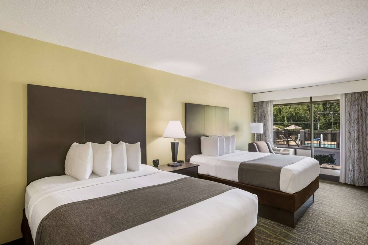 A hotel room with two beds, a large window, and a view of the outdoors.