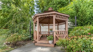 A wooden gazebo with a bench and potted plants, surrounded by lush greenery and flowers. - Best Western Asheville Blue Ridge Parkway (Asheville)