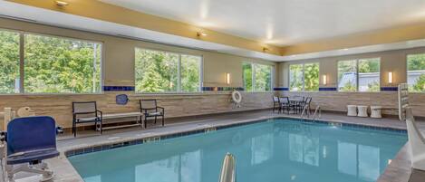 A swimming pool with clear blue water, surrounded by beige walls and large windows.