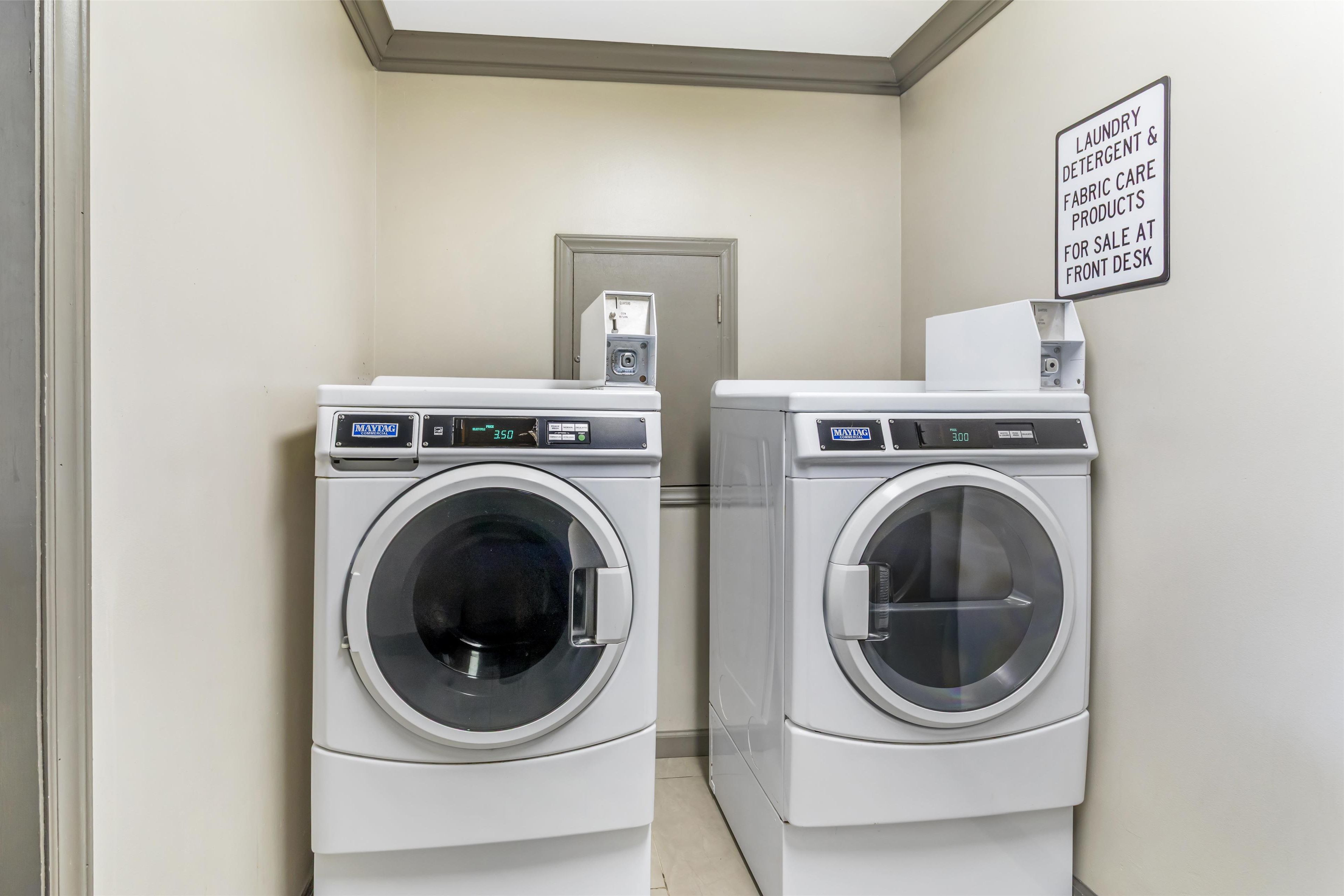 A laundry room with two front-loading washing machines and a sign indicating laundry detergent and fabric care products for sale at the front desk.