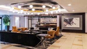 A modern lobby with a black sofa, yellow armchairs, a coffee table, and a bookshelf. - Sheraton Ann Arbor Hotel (Ann Arbor)