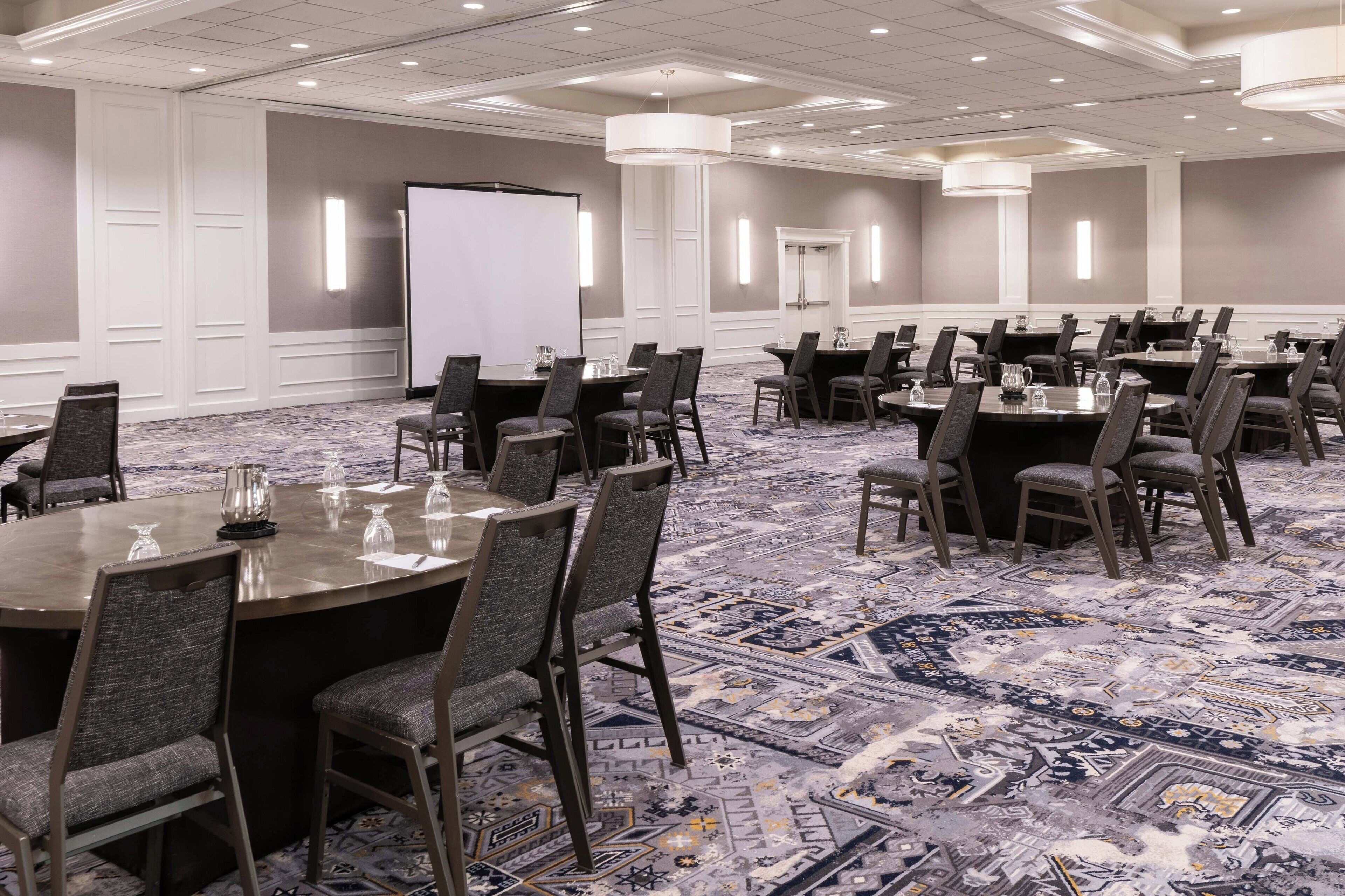 A conference room with multiple tables and chairs, a whiteboard, and a projector screen.