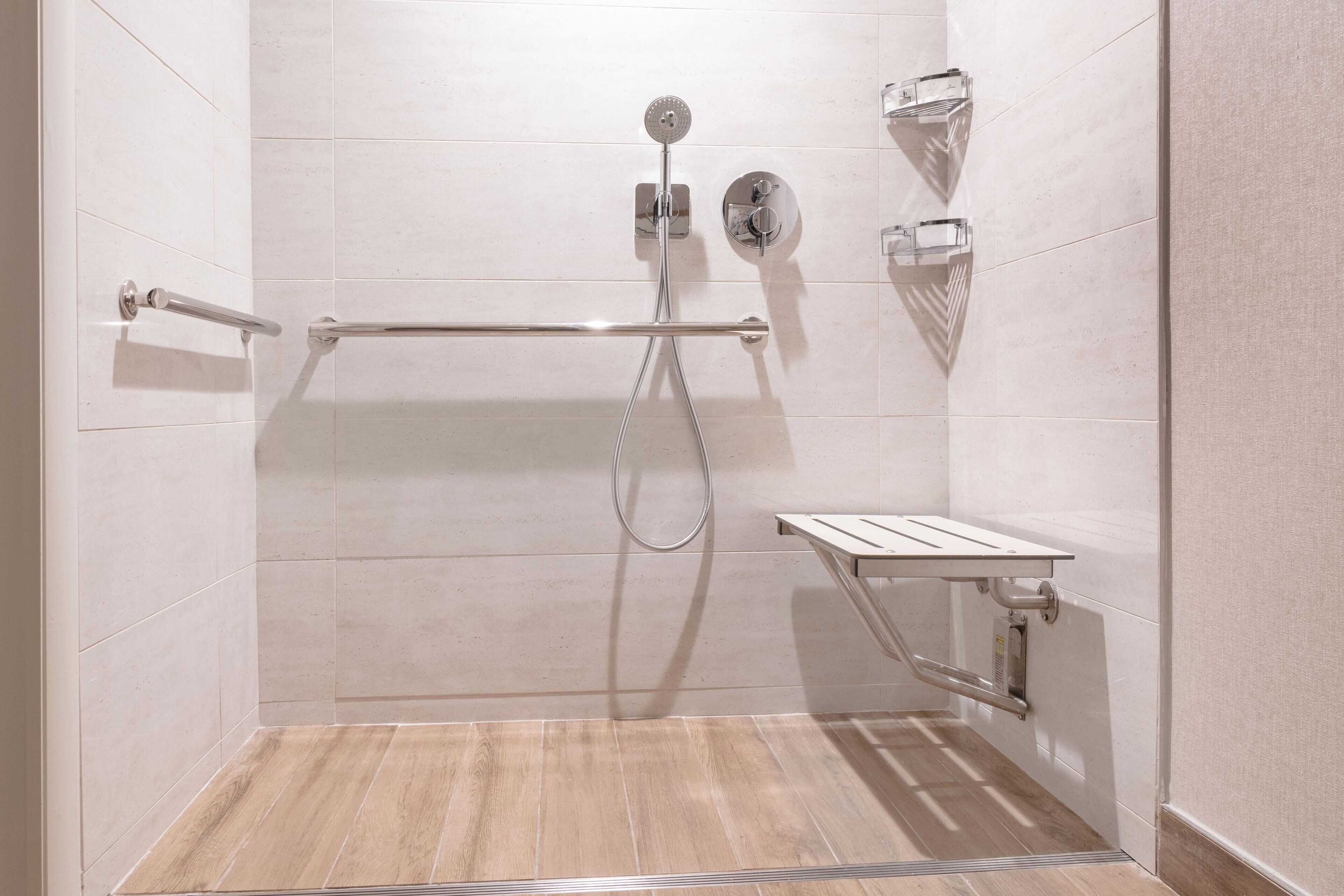 A modern shower area with a grab bar, a handheld showerhead, and a wall-mounted control panel.