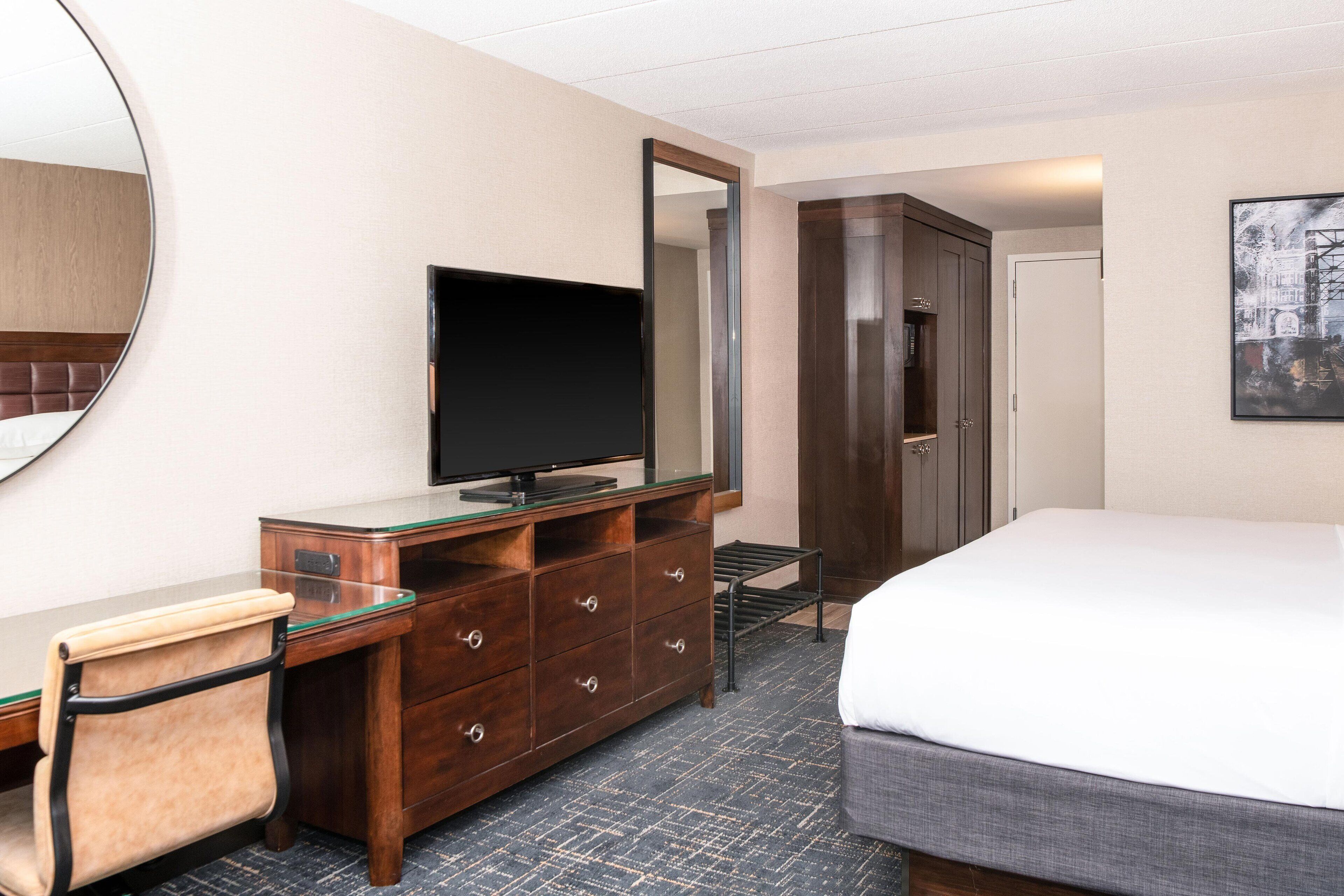 Une chambre d’hôtel comprenant un lit, un bureau avec une chaise, une télévision, une armoire et un miroir.
