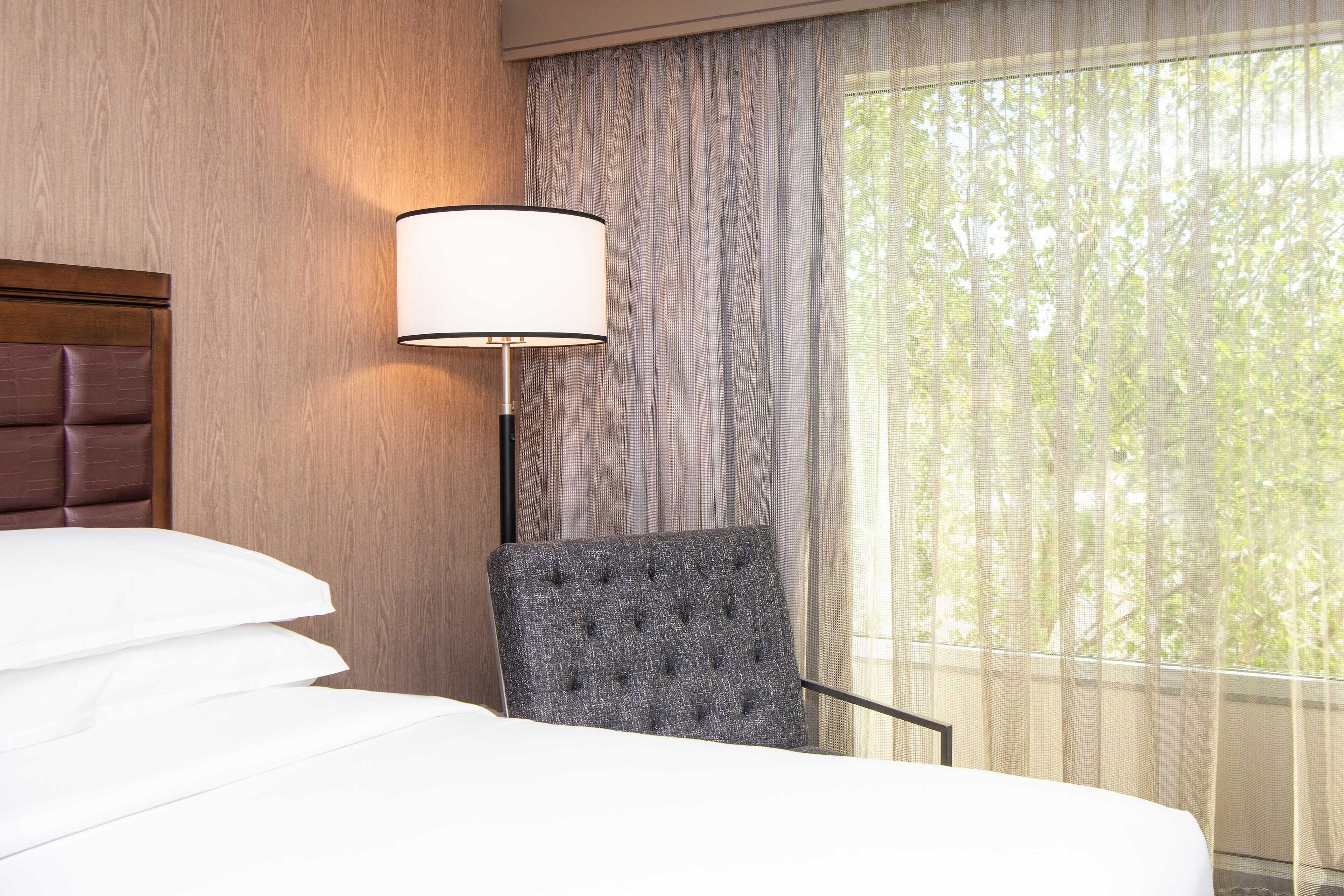A hotel room with a bed, a chair, a lamp, and a window with curtains.