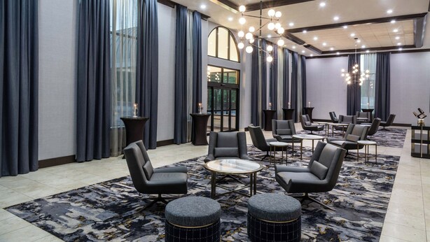 A modern hotel lobby with a marble floor, leather seating, a chandelier, and large windows with curtains. - Sheraton Ann Arbor Hotel (Ann Arbor)