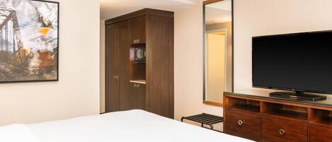 A hotel room with a bed, a television, a wardrobe, and a framed picture on the wall.