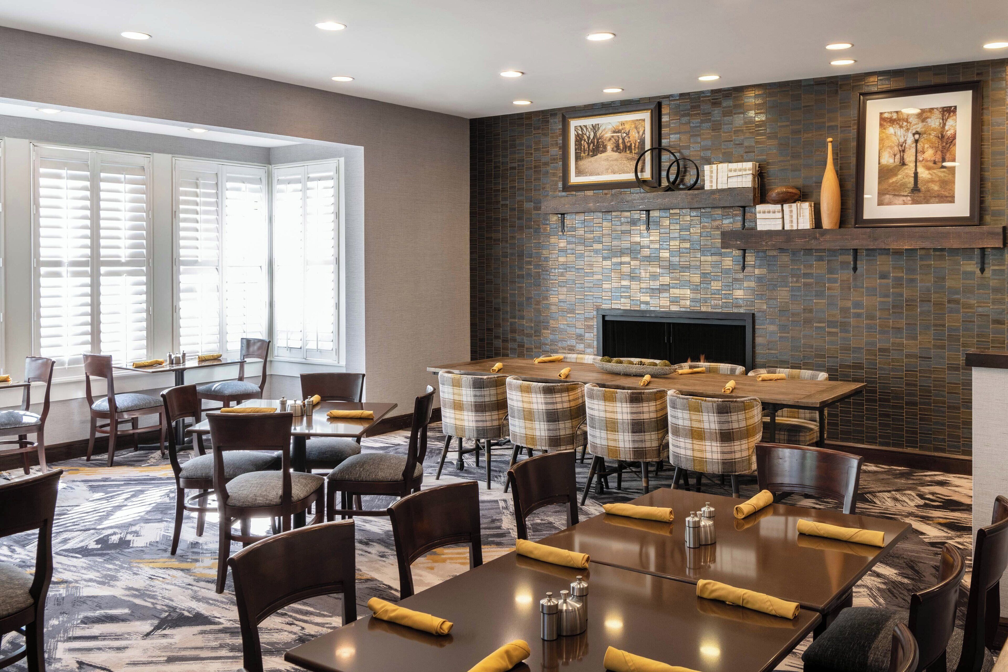 A hotel dining area with multiple tables and chairs, a fireplace, and artwork on the walls.