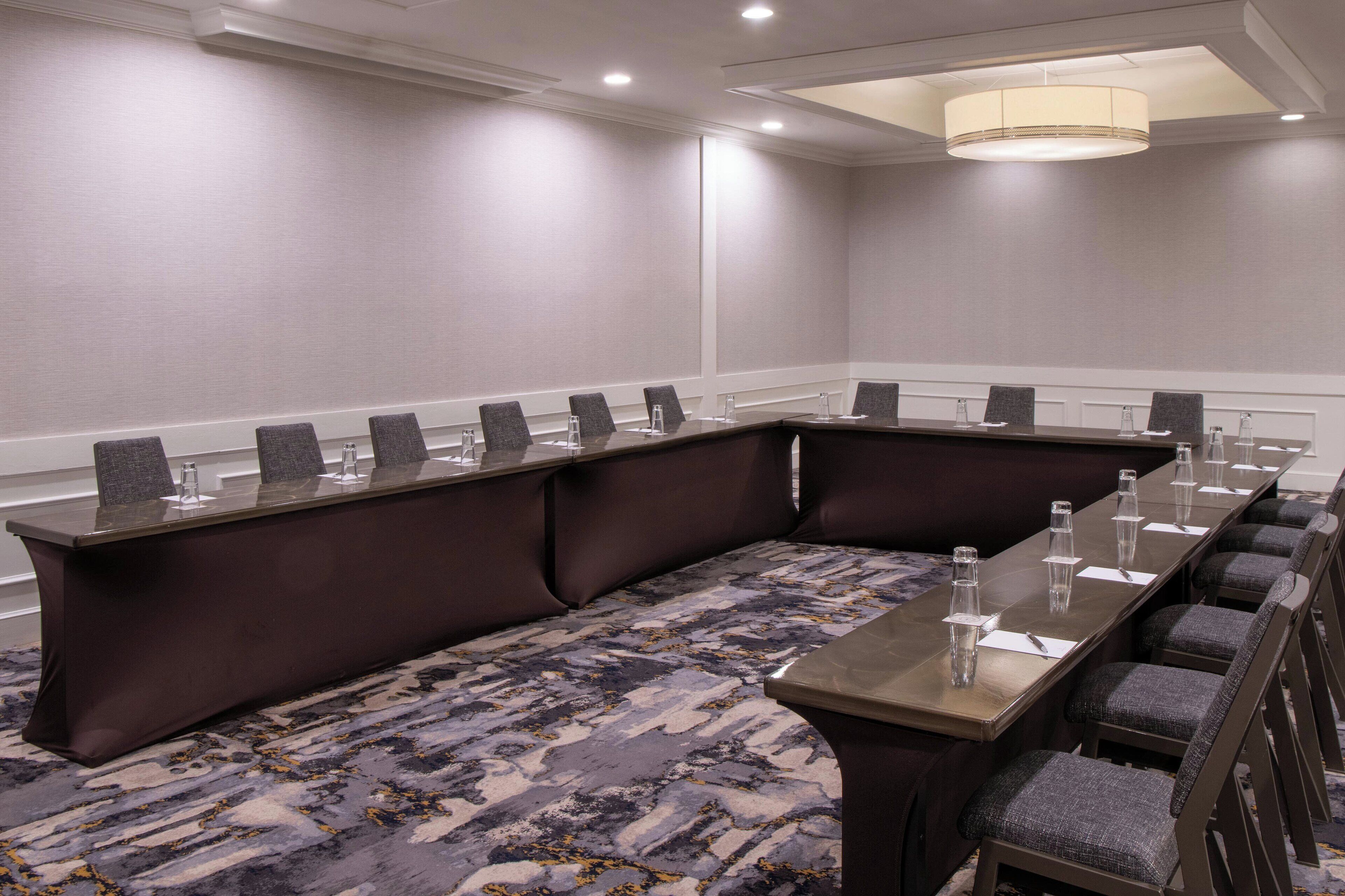 Un salón de conferencias con una larga mesa, varias sillas y piso alfombrado.