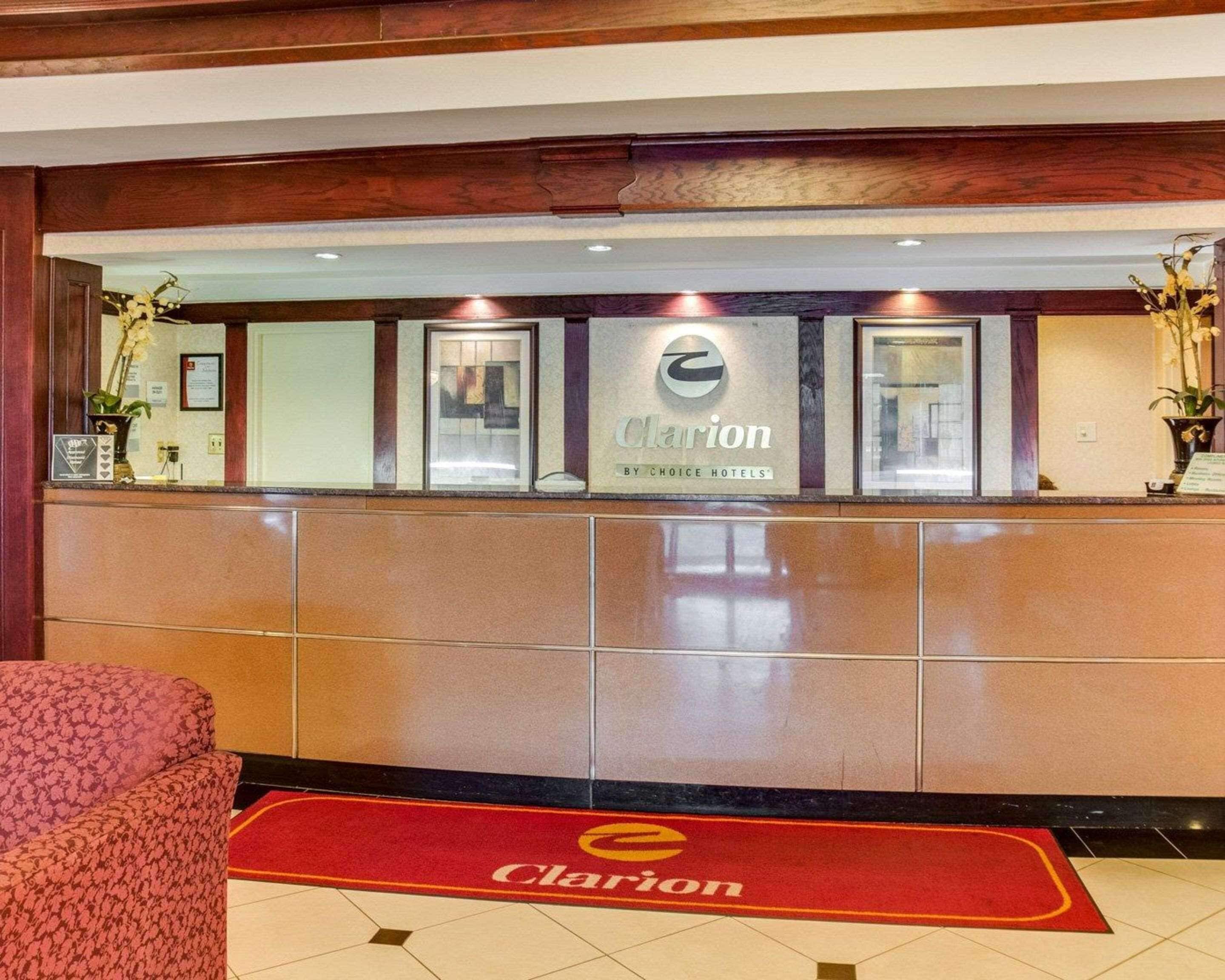 A hotel reception area with a marble counter, a red carpet with the hotel logo, and a floral arrangement on the left.