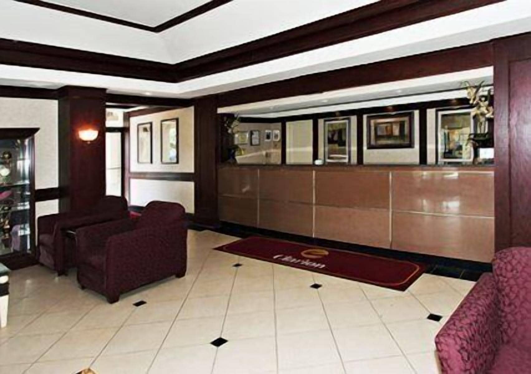 Eine Hotlellobby mit einer Rezeption, gerahmten Bildern an der Wand und einem roten Teppich, der zur Rezeption führt.
