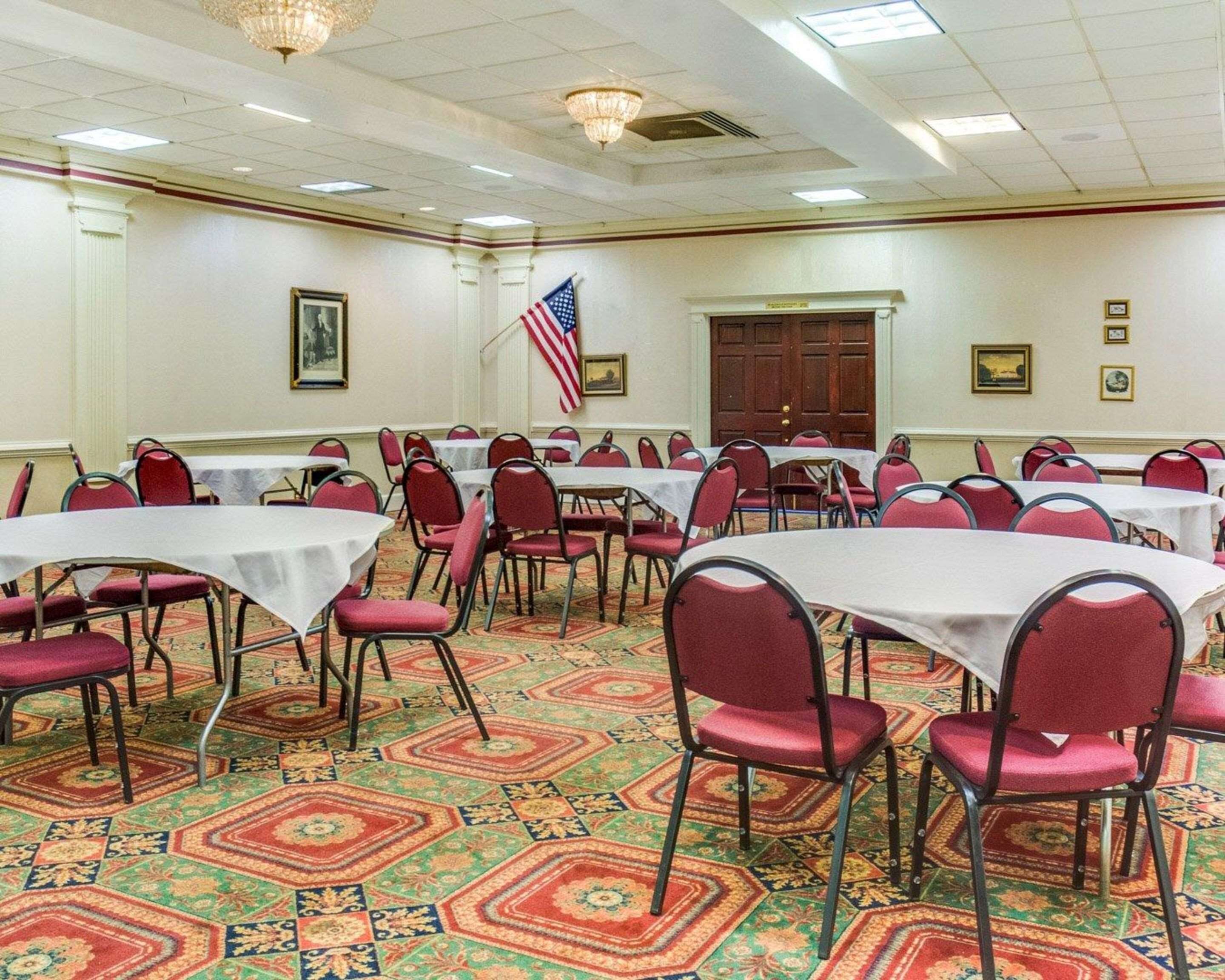 A conference room with multiple tables and chairs, an American flag, and a patterned carpet.
