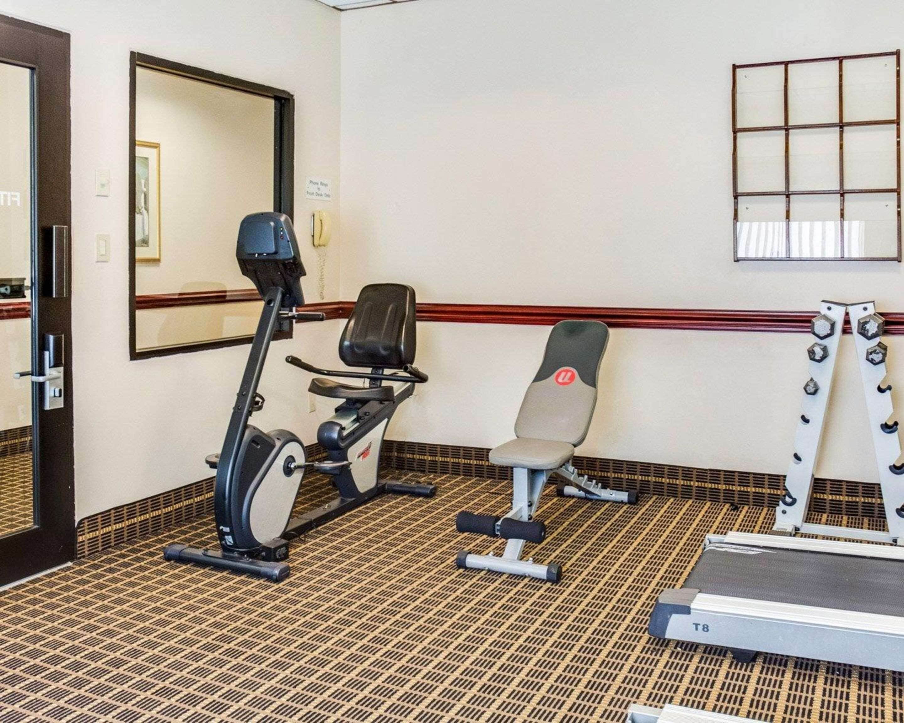 A hotel room with a treadmill, an elliptical machine, and a bench.