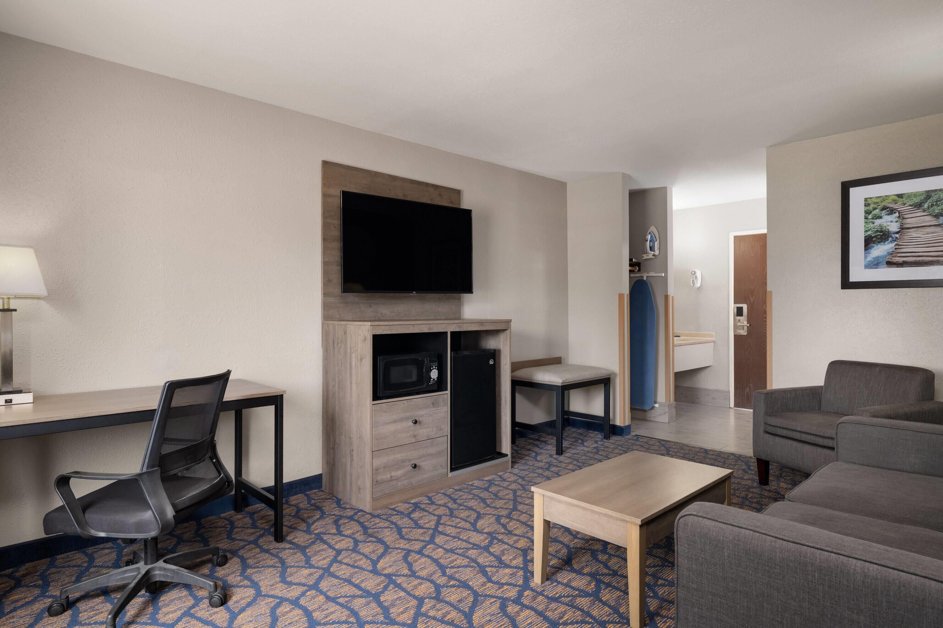 Ett hotellrum med skrivbord, stol, TV, mikrovågsugn och en sittgrupp.