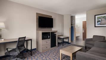 A hotel room with a desk, chair, television, microwave, and seating area.