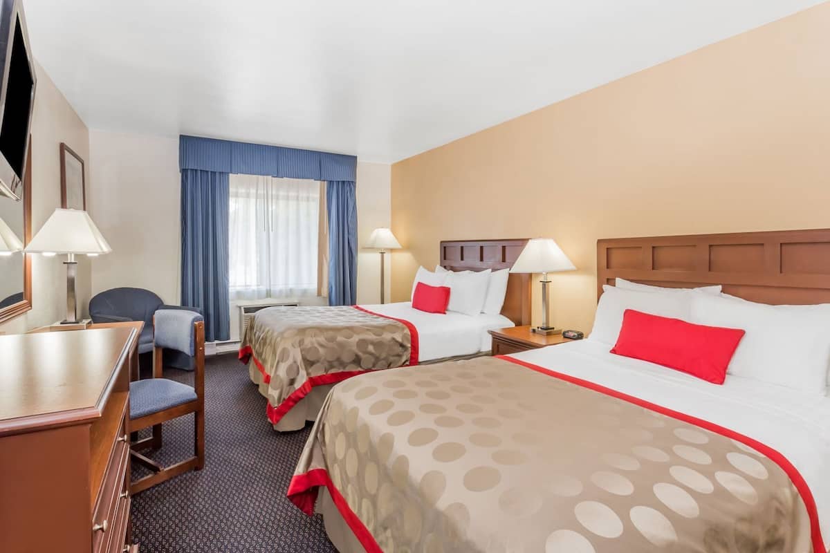 A hotel room with two beds, a desk, a chair, and a television.