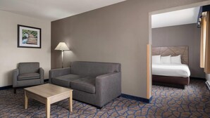 Una habitación de hotel con sofá, sillón, cama y una pequeña mesa.