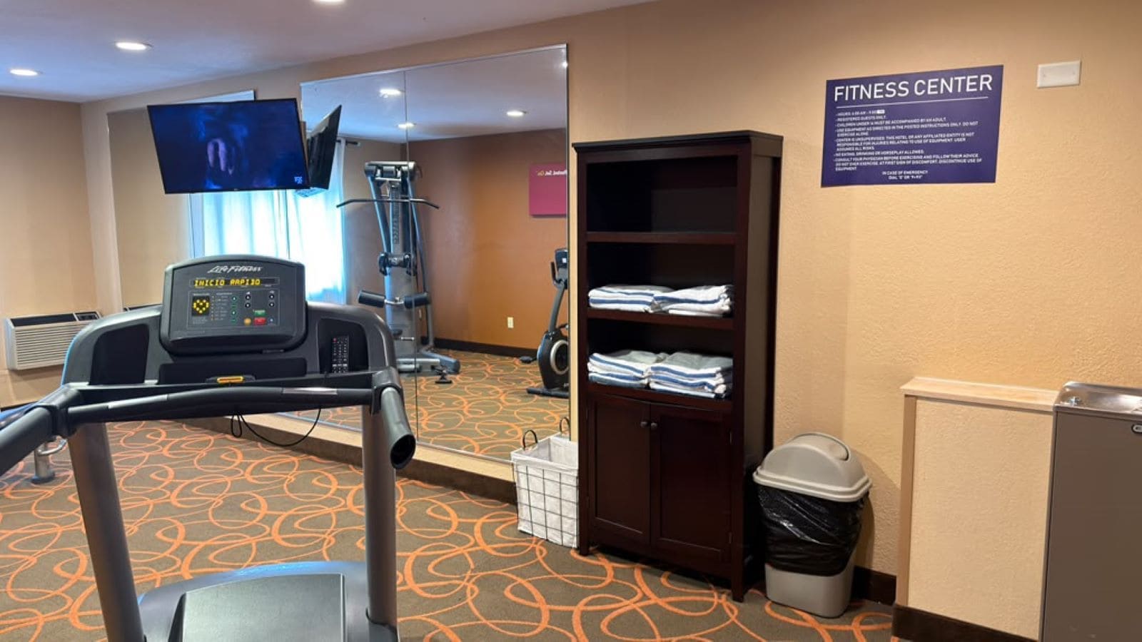 A fitness center with exercise equipment, a mirrored wall, and a sign indicating the location.