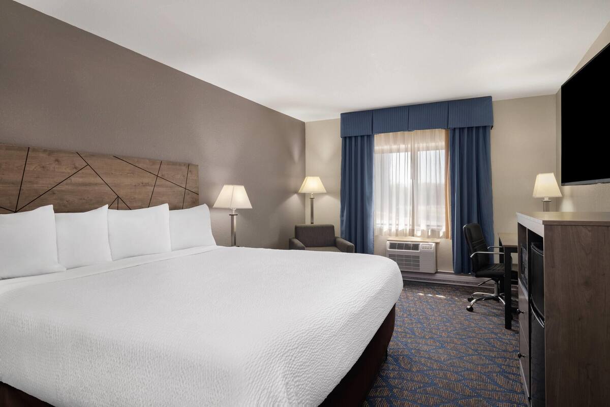 A hotel room with a large bed, two bedside lamps, a desk with a chair, and a television.