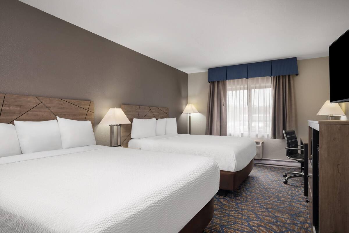 A hotel room with two beds, a desk, a chair, a television, and a window with curtains.