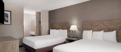 A hotel room with two beds, a desk, a lamp, and a mirror.