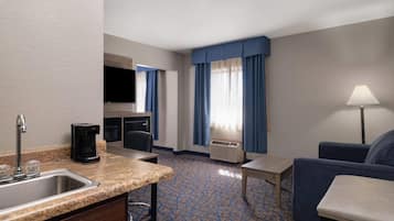 Een hotelkamer met een keukenhoek, een zithoek met een bank en een tafel, en een aan de muur bevestigde televisie.