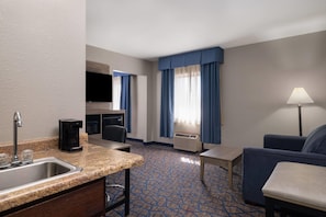 A hotel room with a kitchen area, a seating area with a couch and a table, and a TV mounted on the wall. - Baymont by Wyndham Waukesha (Waukesha)
