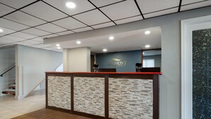 Un mostrador de recepción con un separador de ladrillo, una escalera a la izquierda y un cartel en la pared para Baymont Inn & Suites.