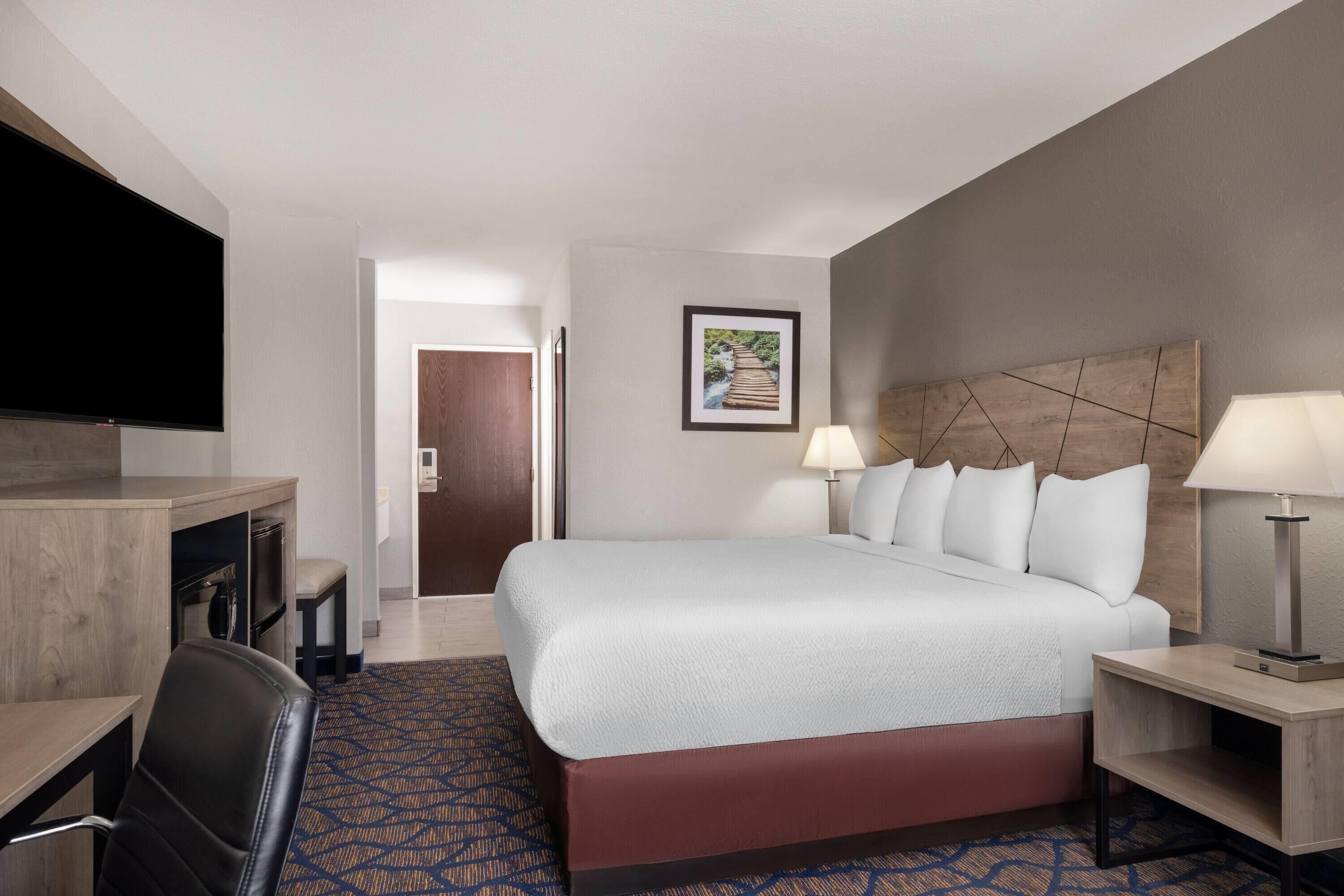 A hotel room with a bed, desk, chair, lamps, and a television.