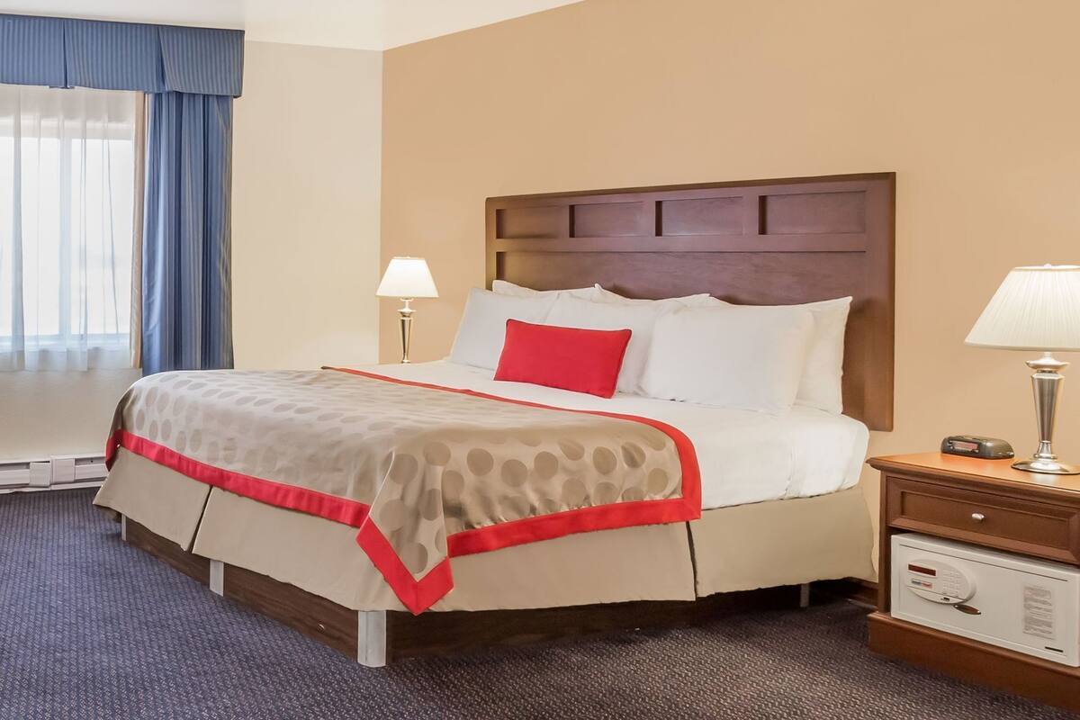 A hotel room with a bed, bedside lamps, a nightstand with a lamp, and a thermostat.