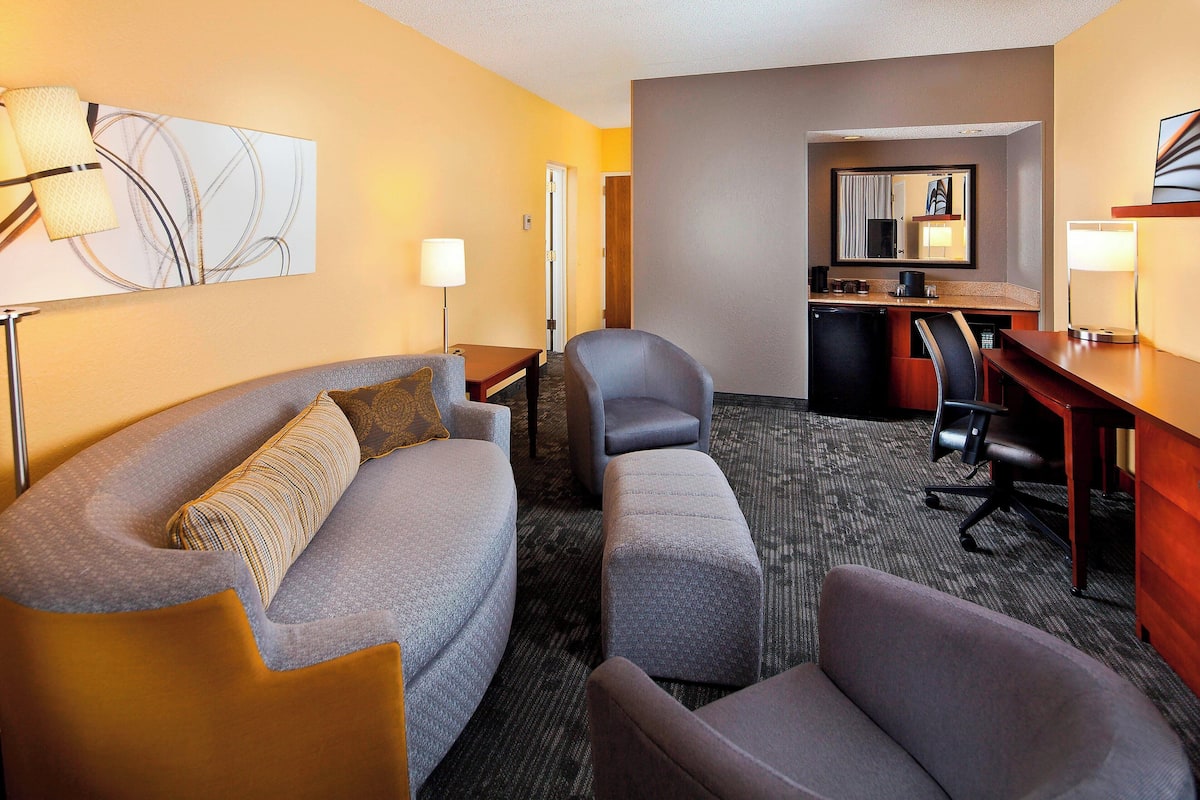 A hotel room with a sofa, two armchairs, a desk, and a kitchenette.