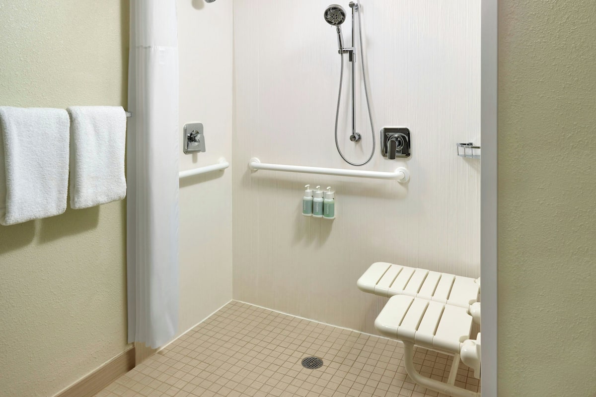 A bathroom with a shower, grab bars, a toilet, and a towel rack.