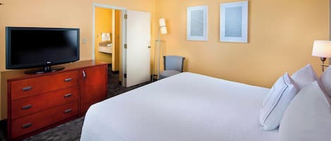A hotel room with a large bed, a flat-screen TV on a wooden dresser, a chair, and two framed pictures on the wall.