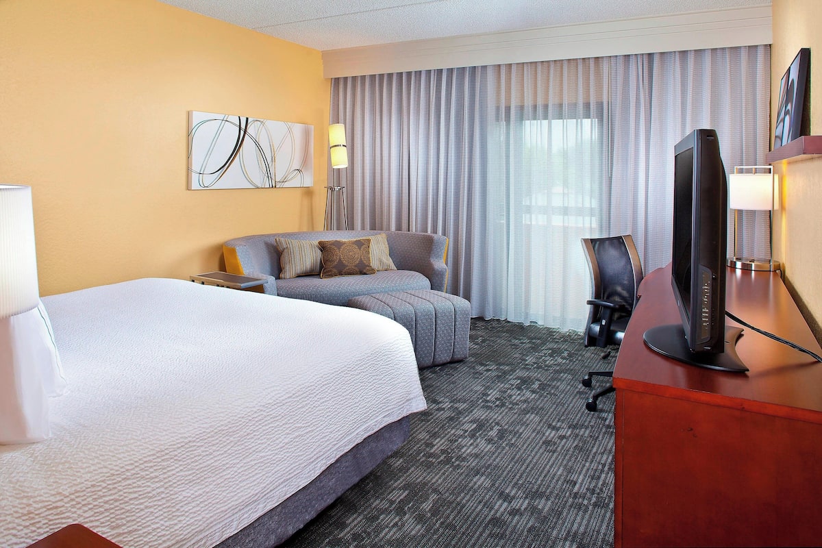 A hotel room with a large bed, a sofa, a desk with a computer, and a TV.