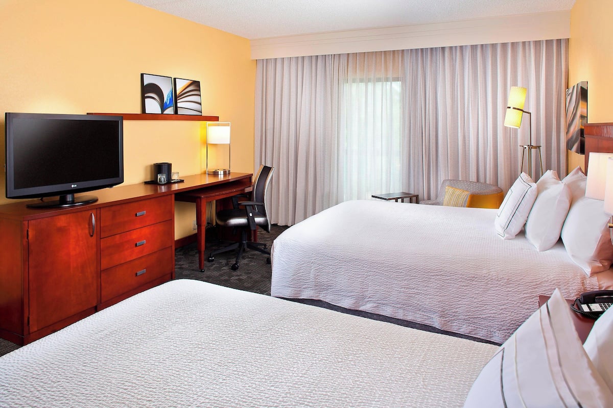 A hotel room with two beds, a desk with a television, a chair, and a lamp.