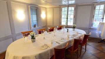 Ein Esszimmer mit einem runden Tisch, gedeckt für sechs Personen, weißen Tischdecken und roten Stühlen.