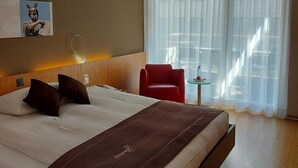 Una camera d'albergo con un letto grande, una poltrona rossa, un tavolino e un quadro appeso al muro.