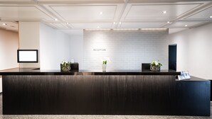 Una reception con piano in legno scuro, parete a mattoni bianchi e insegna con la scritta 'RECEPTION'.