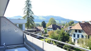 Un balcone con ringhiera affacciato su una zona residenziale con case e una montagna sullo sfondo.