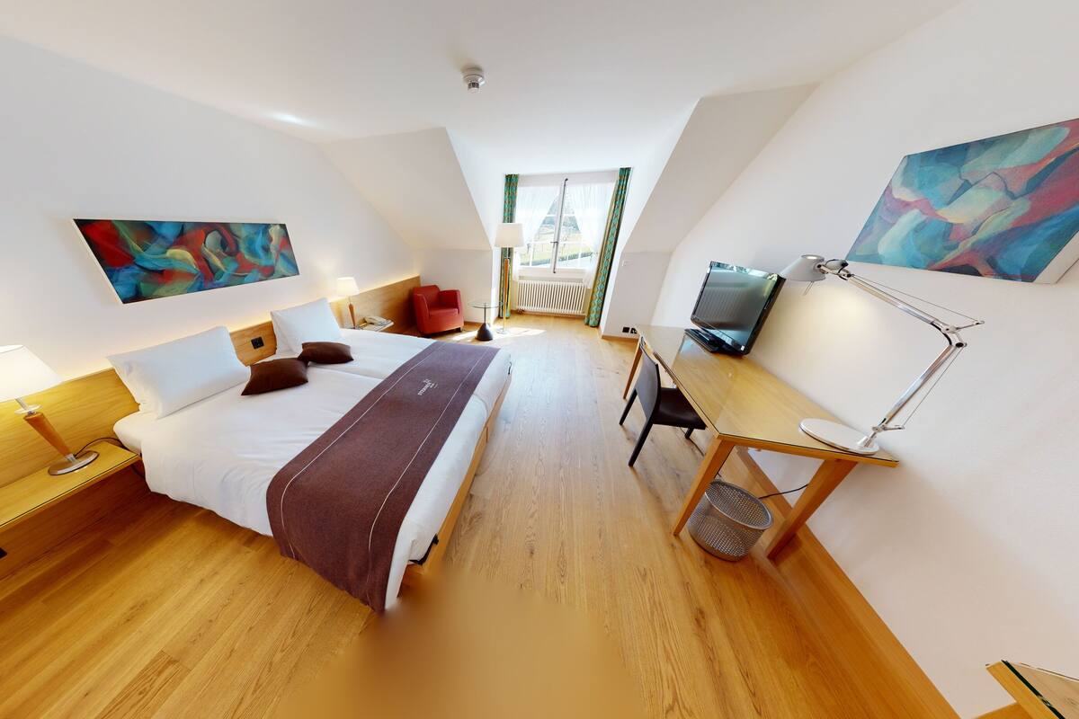 Una habitación de hotel moderna con una cama grande, un escritorio con ordenador, televisor y obras de arte en las paredes.