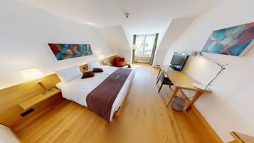 A modern hotel room with a large bed, a desk with a computer, a TV, and artwork on the walls.