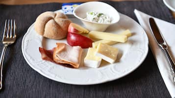 Un plato con diversos alimentos, como pan, manzanas, queso y un pequeño recipiente con salsa, sobre una mesa con un mantel individual.