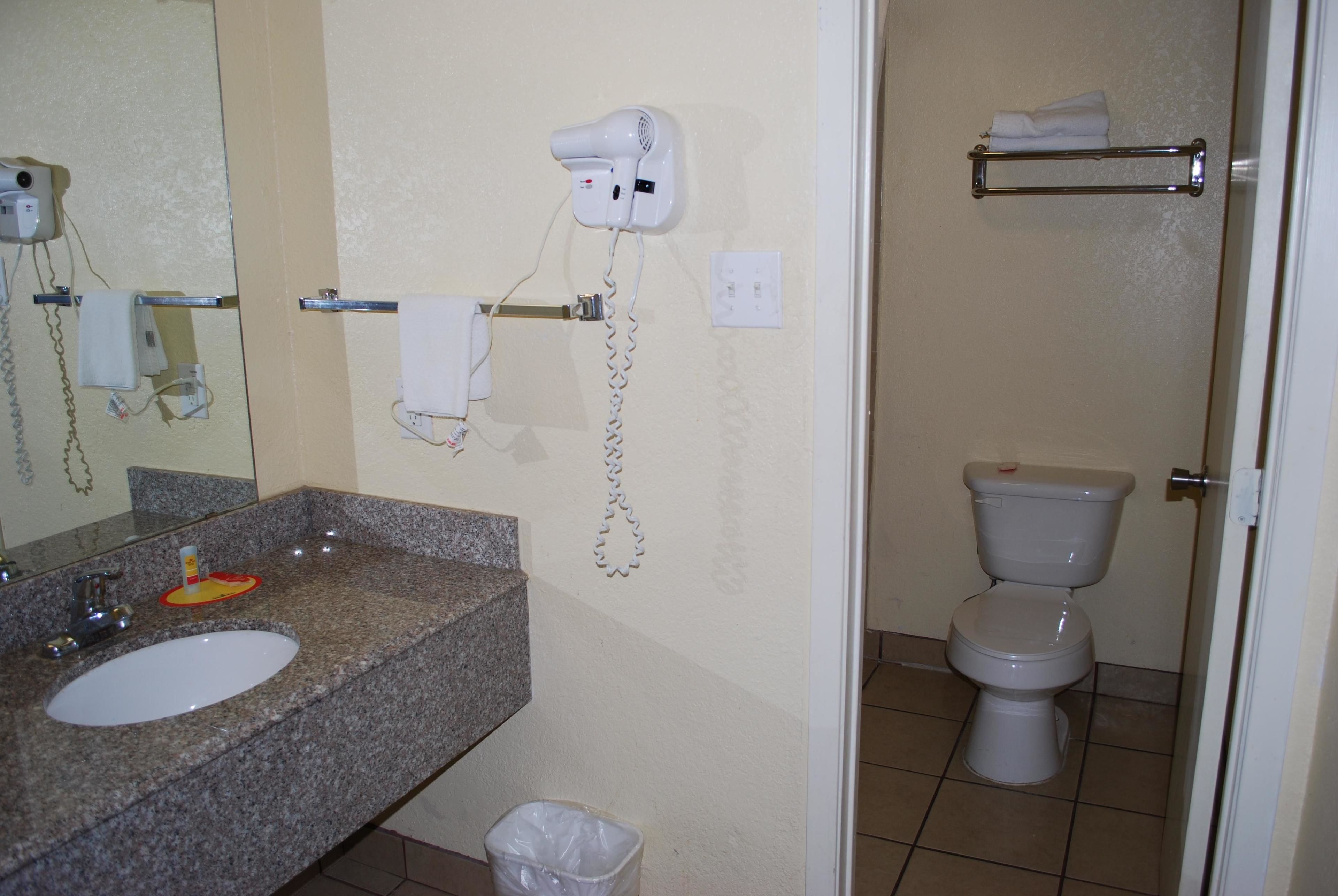 Un baño con lavamanos de encimera de granito, un secador de pelo, un perchero y un inodoro.