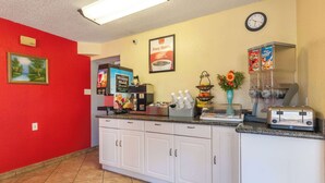 A kitchen with white cabinets, a red wall, a clock, and various appliances including a coffee maker and a toaster. - Econo Lodge San Marcos University Area (San Marcos)
