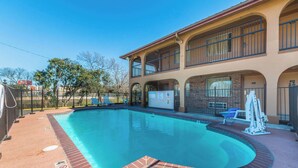 A swimming pool with a brick border, a covered area with a roof, and a building with multiple balconies and windows. - Econo Lodge San Marcos University Area (San Marcos)