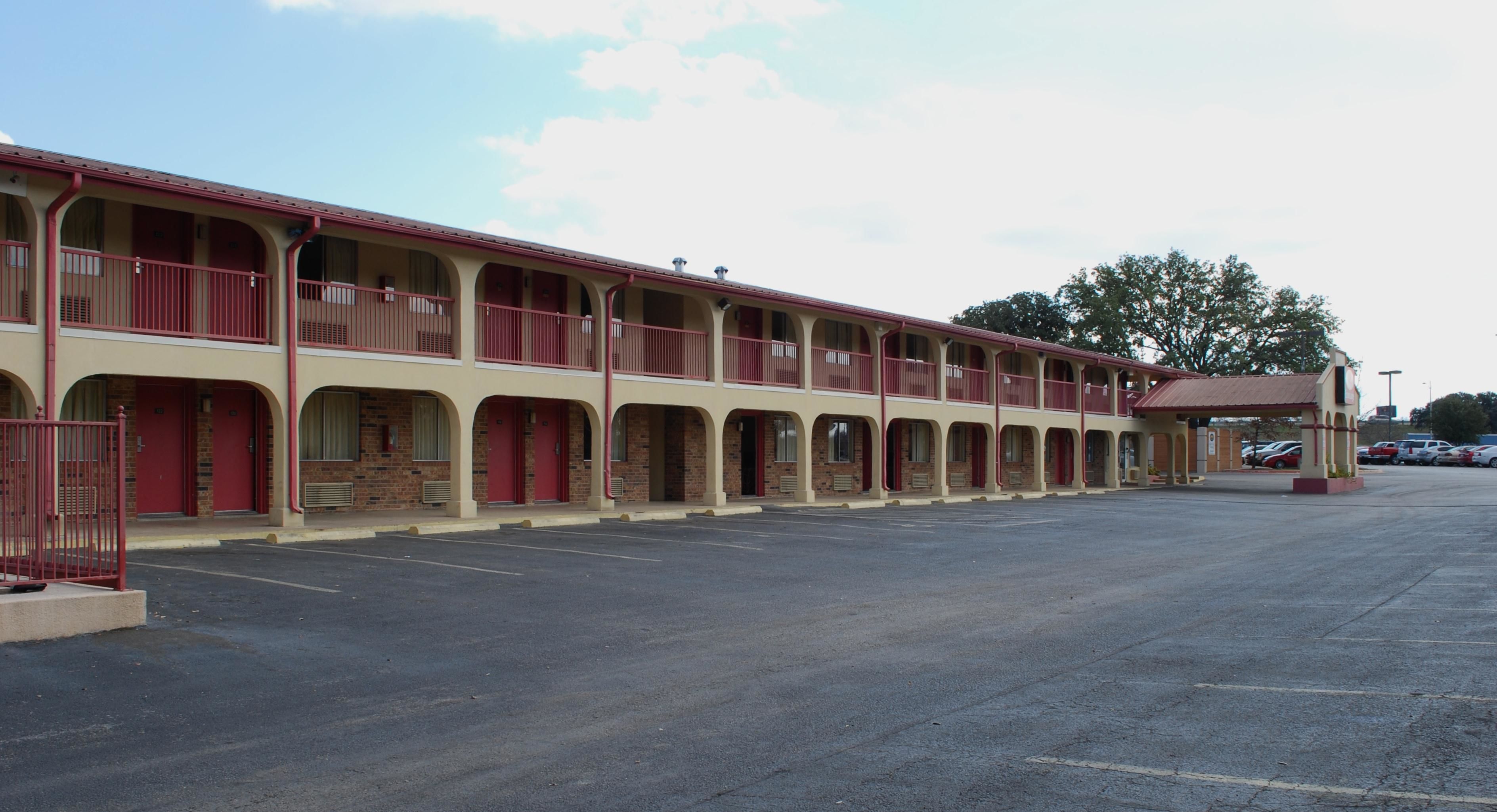 A motel with multiple rooms, a covered parking area, and a row of parked cars.