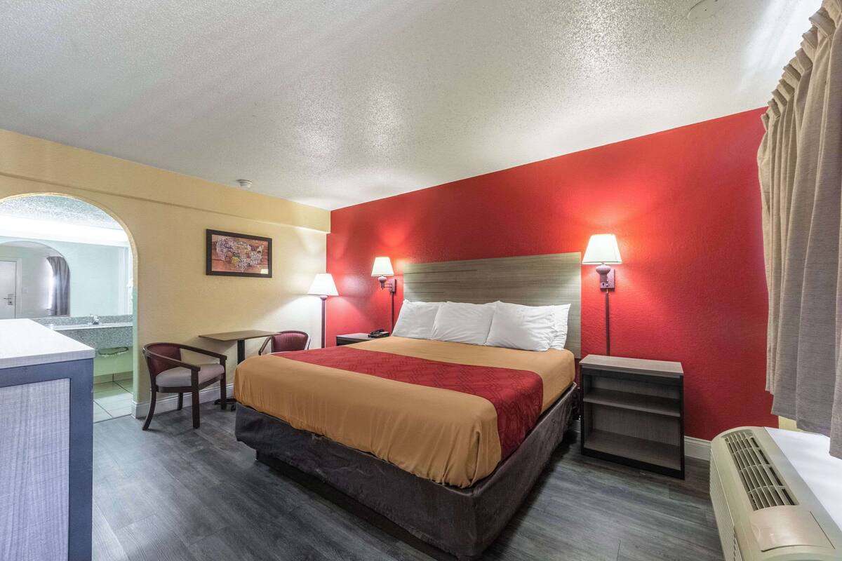 Habitación de hotel con cama, dos lámparas de noche, un escritorio, una silla y un espejo.