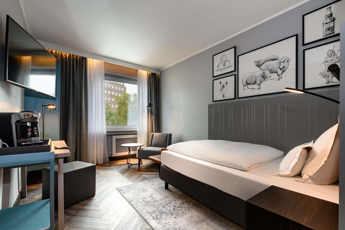 Une chambre d’hôtel moderne équipée d’un lit, d’un bureau, d’une machine à café et ornée d’œuvres d’art sur les murs.