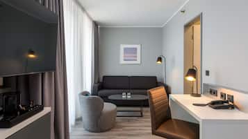 Ein modernes Hotelzimmer mit Flachbildfernseher, einer Couch, einem Schreibtisch mit Telefon und einem Sessel.