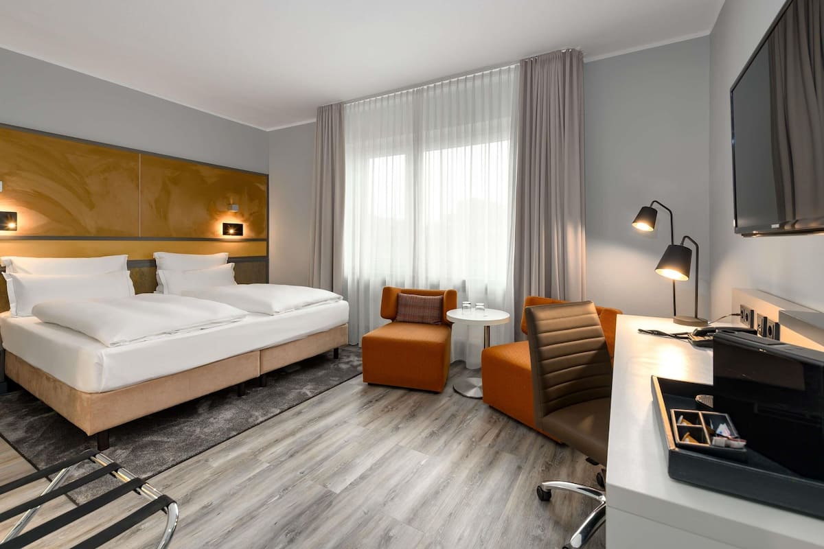 Une chambre d’hôtel comprenant un lit, un bureau avec une chaise, une petite table et un téléviseur.
